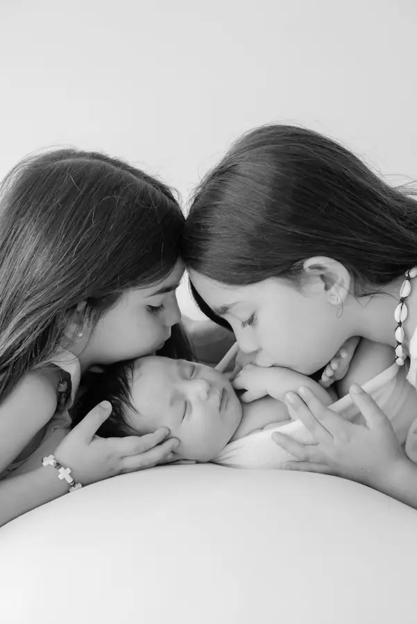 Dos hermanas dando un beso a su hermano recién nacido